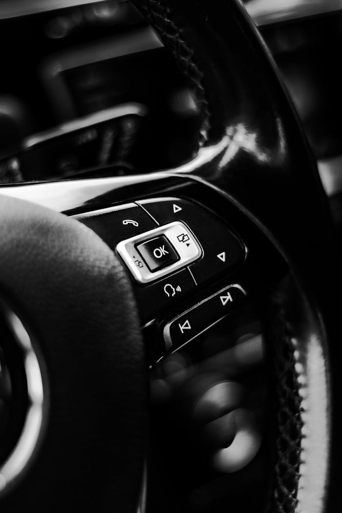 about-me-02 A detailed black and white close-up of modern car steering wheel controls, showcasing sleek design.